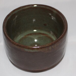 May include: A small, brown ceramic bowl with a green glaze inside. The bowl has a slightly textured exterior.