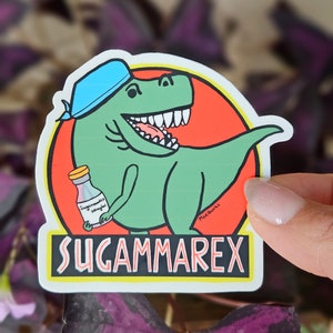 Puede incluir: Un dinosaurio verde con un pa&ntilde;uelo azul sostiene una botella de "Sugammarex Vitamins" en su mano. El dinosaurio sonr&iacute;e con la boca abierta, mostrando sus dientes. La pegatina est&aacute; sobre un fondo rojo con un borde amarillo y el texto "Sugammarex" en una fuente en blanco y negro.