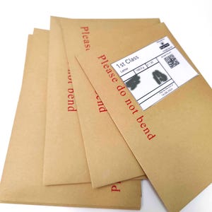 May include: A stack of brown paper envelopes with the words "Please do not bend" printed in red. One envelope has a white shipping label with a barcode and text. The envelopes are on a white background.