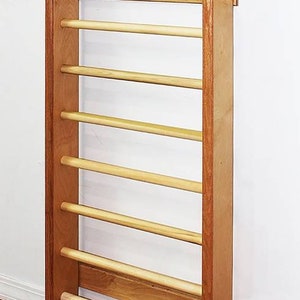 May include: A wooden wall-mounted pull-up bar with seven rungs. The bar is made of light brown wood with dark brown accents. The bar is mounted to a white wall.