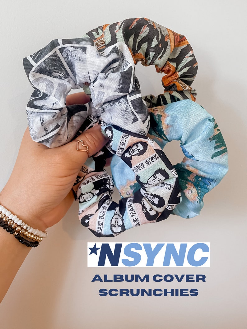 May include: A collection of three scrunchies with various patterns. One scrunchie features a black and white image, another has a blue and green design with text, and the third has a brown and orange pattern. The text "*NSYNC ALBUM COVER SCRUNCHIES" is displayed.