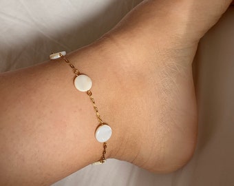 May include: A gold chain anklet with white round shell charms.