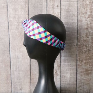 Peut inclure: Un bandeau à nœuds de couleur violet, rose, jaune et turquoise. Le bandeau est sur une tête de mannequin noire.