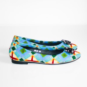 Puede incluir: Un par de bailarinas de ballet con estampado azul, verde, amarillo y rojo con un adorno negro de joyas en la punta.