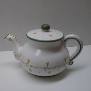 May include: White ceramic teapot with a green lid and handle. The teapot is decorated with a green and yellow floral pattern.