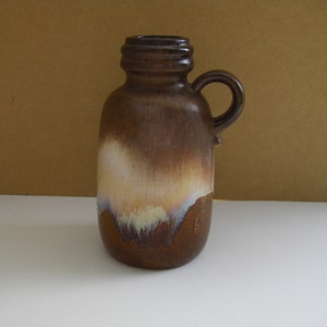May include: A brown ceramic vase with a white and yellow glaze. The vase has a handle and a rounded body.
