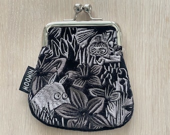 May include: A black velvet coin purse with a silver metal clasp and embroidered floral and creature designs. The purse has a black label with the word "NOOMIN" printed in white.