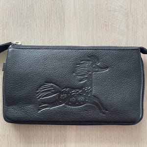 Pode incluir: Uma clutch de couro preto com um z&iacute;per prateado e um design decorativo em relevo de um cavalo estilizado.