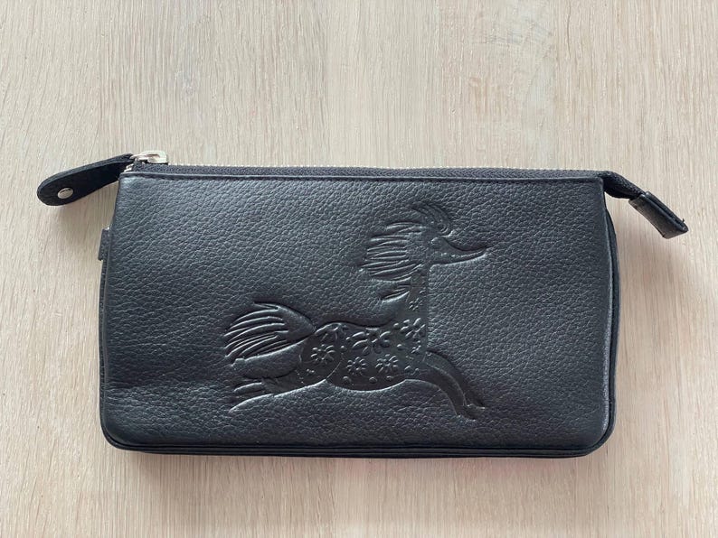 Pode incluir: Uma clutch de couro preto com um z&iacute;per prateado e um design decorativo em relevo de um cavalo estilizado.