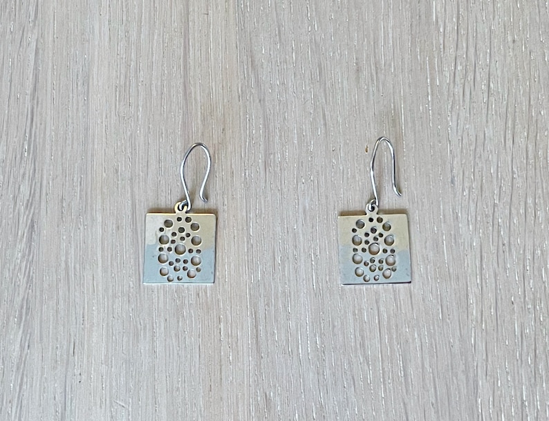 May include: A pair of silver earrings with a square shape and a cutout design of small circles.