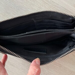 Pode incluir: Carteira de couro preta com fecho de correr e v&aacute;rios compartimentos. A carteira est&aacute; aberta para revelar o forro interior.