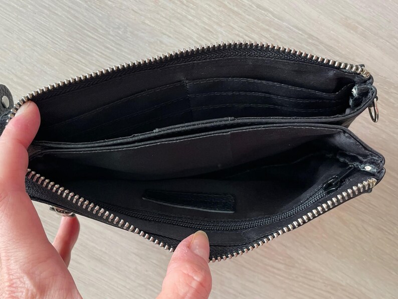 Pode incluir: Carteira de couro preta com fecho de correr e v&aacute;rios compartimentos. A carteira est&aacute; aberta para revelar o forro interior.