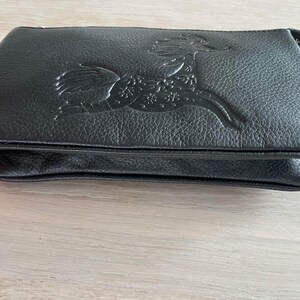 Pode incluir: Uma clutch de couro preto com um design em relevo detalhado de um animal estilizado com acentos florais.