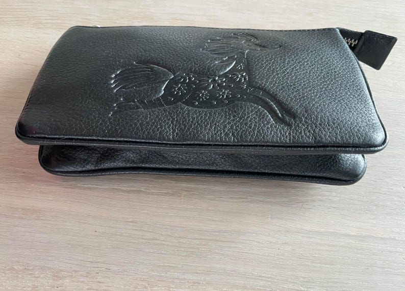 Pode incluir: Uma clutch de couro preto com um design em relevo detalhado de um animal estilizado com acentos florais.