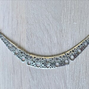 May include: A silver necklace with a geometric design featuring a series of interconnected circles. The necklace is made of a metal chain and has a modern, minimalist style.