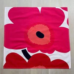 May include: A white tea towel with a pink floral pattern. The flowers have a red center and a black dot in the middle.