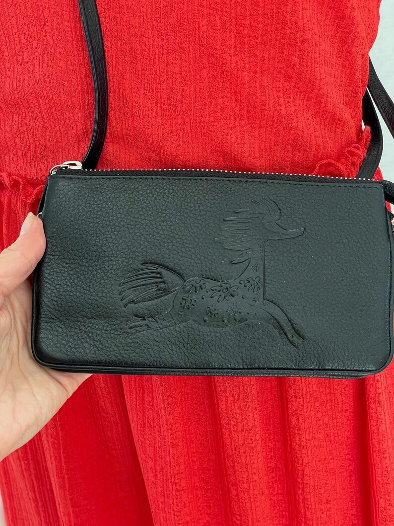 Pode incluir: Bolsa de ombro de couro preto com z&iacute;per prateado e um design de cavalo em relevo detalhado na frente.