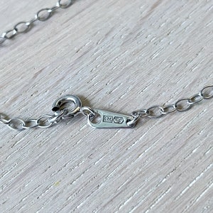 May include: Close-up of a silver chain necklace with a clasp. The clasp has a small rectangular tag with the inscription "925" on it.