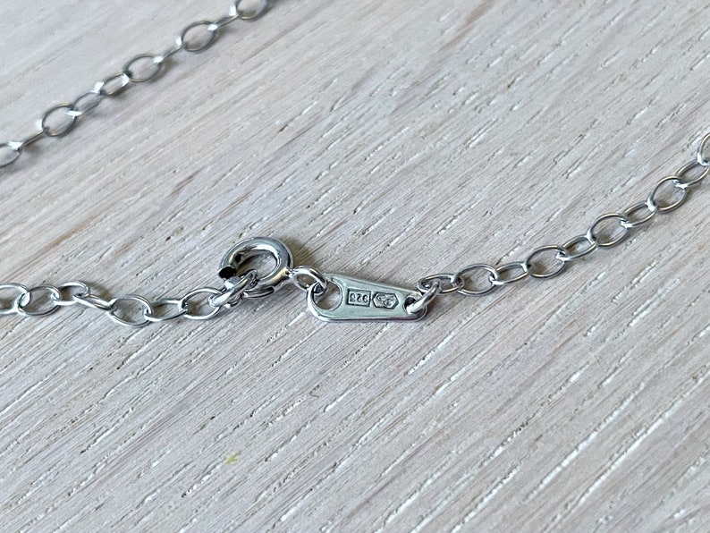May include: Close-up of a silver chain necklace with a clasp. The clasp has a small rectangular tag with the inscription "925" on it.