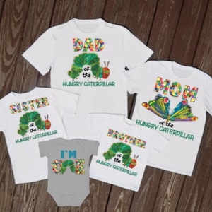 Puede incluir: Un conjunto de cinco camisetas blancas con el tema de La Oruga Muy Hambrienta. Las camisetas presentan el texto "Pap&aacute;", "Mam&aacute;", "Hermana", "Hermano" y "Tengo un a&ntilde;o" con un gr&aacute;fico de oruga.