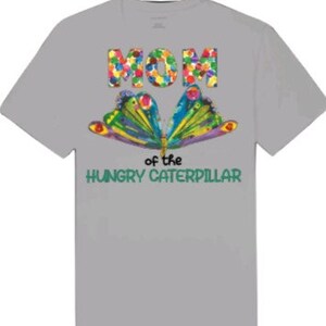 Puede incluir: Camiseta gris con una mariposa colorida y el texto "Mam&aacute; de la oruga hambrienta" impreso en ella.