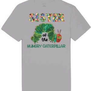Puede incluir: Camiseta gris con un gr&aacute;fico colorido de "Hermana de la Oruga Hambrienta". La oruga es verde con una cabeza roja y est&aacute; rodeada de flores coloridas.