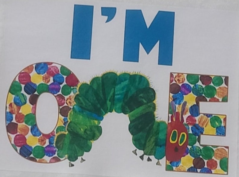 Puede incluir: Una pancarta de cumplea&ntilde;os colorida con las palabras "I'M ONE" en letras azules. Las letras O y E est&aacute;n hechas de c&iacute;rculos coloridos, y la letra N es una oruga verde.
