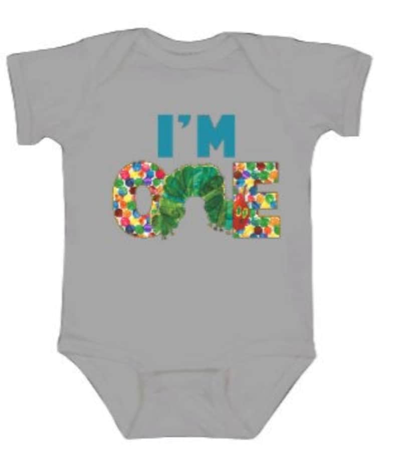 Puede incluir: Un body de beb&eacute; gris con las palabras "I'm One" en azul y verde. El n&uacute;mero uno est&aacute; formado por una oruga verde con puntos de colores.
