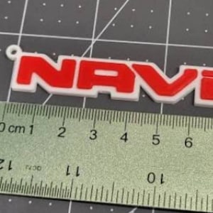May include: A white plastic keychain with a red "NAVI" logo. The keychain is about 5 cm long.