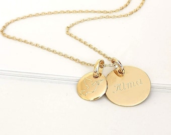 Op de afbeelding: Gouden ketting met twee bedels. Een bedel is een kleine cirkel met een vogelontwerp. De andere bedel is een grotere cirkel met de naam "Alma" erop gegraveerd.
