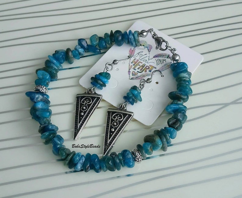 May include: A turquoise blue chip stone bracelet and matching earrings with silver triangle pendants. The earrings have silver hooks. The bracelet has a silver clasp. The earrings and bracelet are on a white card with the text "Believe Your Heart".
