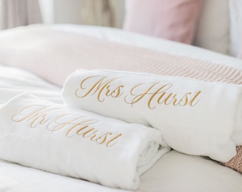 Könnte beinhalten: Zwei weiße Handtücher mit goldener Stickerei. Das obere Handtuch sagt "Mrs. Hurst" und das untere Handtuch sagt "Mr. Hurst".