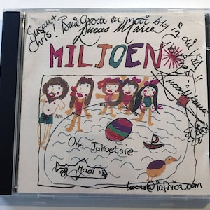 May include: A colorful drawing of a family at the beach with the words "Ons Jakoetsie" and "Haai" written in the water. The drawing is on a white CD case with the title "MILJOEN" written in large, colorful letters. The CD case is signed by Lucas Mare.