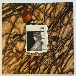 May include: A vintage record album cover with a brown and tan background featuring a photo of a woman with curly hair. The album is titled "Marti Jones Match Game".