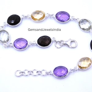 May include: A silver bracelet with oval gemstones in black, yellow, purple, and green. The bracelet is linked with small silver chains and has a clasp. The text "GemsandJewelsIndia" is visible.