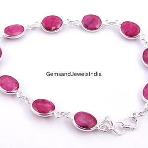 Può includere: Un bracciale in argento con pietre preziose rosse ovali. Le pietre sono incastonate in castoni individuali e collegate con piccoli connettori d'argento. Il bracciale è esposto su una superficie bianca. Il testo "GemsandJewelsIndia" è visibile.