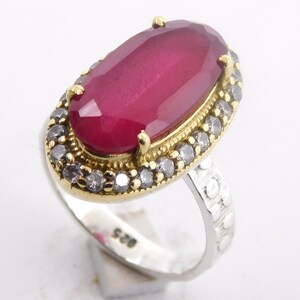 Può includere: Un anello d'argento con una grande pietra ovale rossa circondata da piccole pietre trasparenti. La fascia dell'anello è testurizzata e ha un timbro 925.