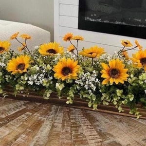 May include: A wooden planter box filled with a floral arrangement of yellow sunflowers and white baby's breath.