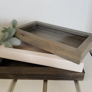 May include: Three wooden trays stacked on top of each other. The top tray is gray, the middle tray is white, and the bottom tray is dark brown.
