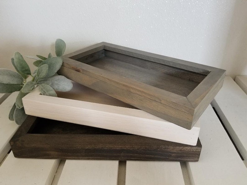 May include: Three wooden trays stacked on top of each other. The top tray is gray, the middle tray is white, and the bottom tray is dark brown.