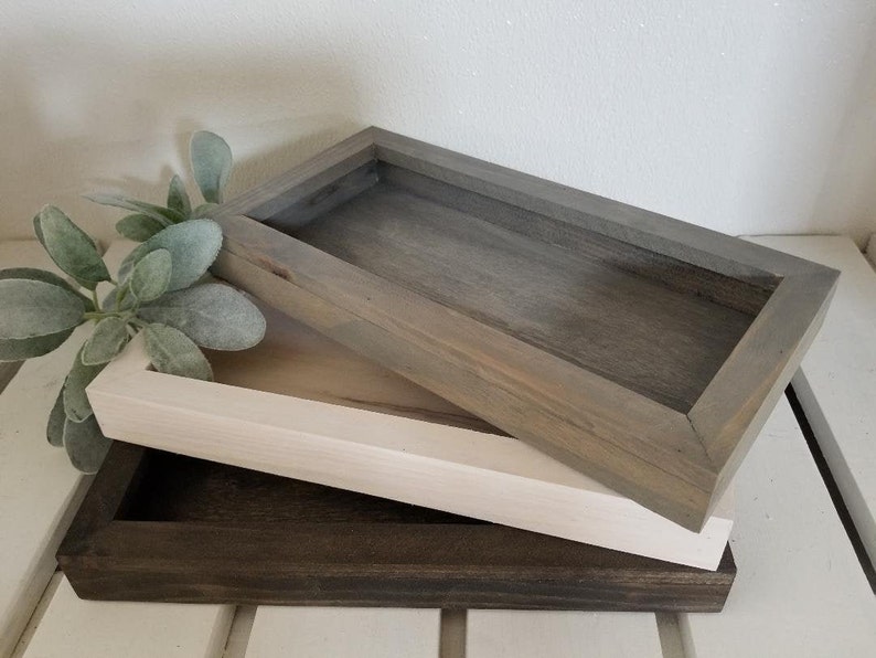 May include: Three wooden trays stacked on top of each other. The top tray is gray, the middle tray is white, and the bottom tray is dark brown.