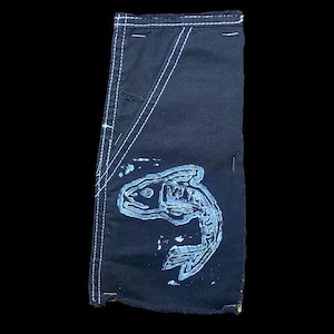 May include: Dark navy blue fabric with a white fish skeleton design. The fabric has white stitching along the edges and a pocket-like design. The fish skeleton is light blue.