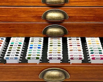 May include: A wooden drawer organizer with multiple drawers, each containing small plastic containers with color swatches. The drawers have brass handles. The top drawer has the initials "DVC" carved into the wood.