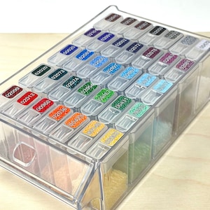 May include: A clear plastic storage box with multiple compartments, each containing small colourful beads. The compartments are labelled with numbers.