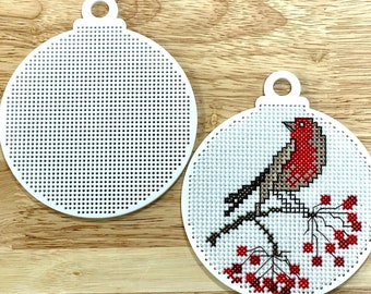 May include: Two white round plastic ornaments for cross-stitch. One ornament is blank and the other has a red-breasted bird with brown wings perched on a branch with red berries.
