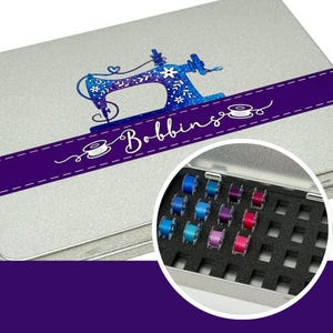 Może przedstawiać: Srebrne metalowe pudełko do przechowywania nici do szycia z wzorem maszyny do szycia z niebieskimi i fioletowymi błyskotkami na pokrywie. Pokrywa ma również fioletową wstążkę z napisem "Bobbinso". Pudełko ma czarną piankową wkładkę z 16 gniazdami do przechowywania szpulek nici do szycia.