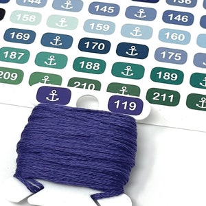 Può includere: Primo piano di un filo da ricamo viola avvolto attorno a un'aspo di plastica bianca. L'aspo è etichettato con il numero "119". L'aspo è circondato da una griglia di quadrati numerati e codificati a colori, ognuno con un simbolo di ancora.