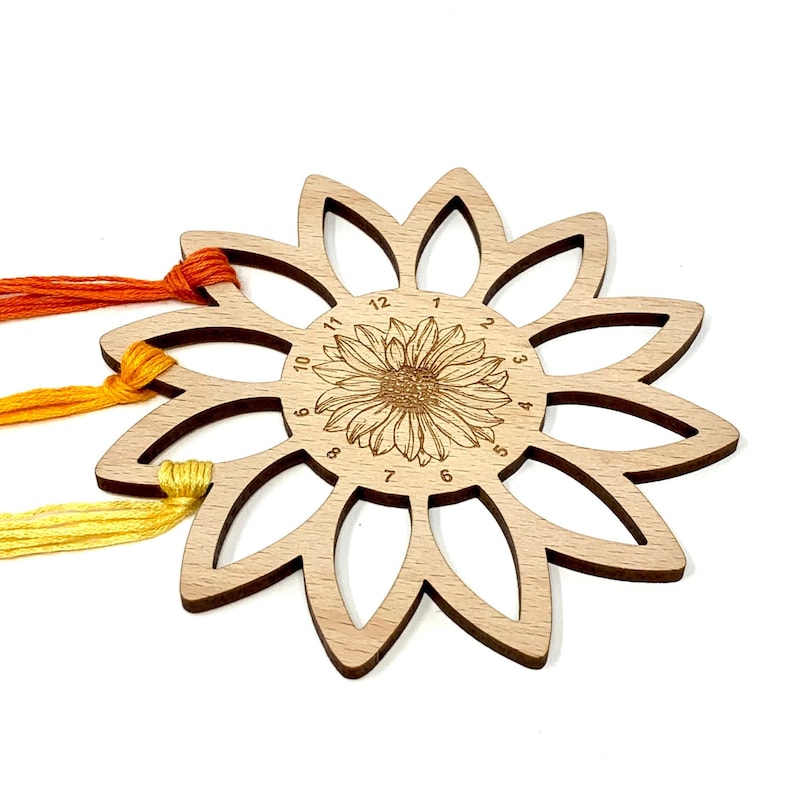 May include: Wooden sunflower-shaped thread organizer with 12 slots for storing embroidery floss. The organizer has a sunflower design in the center with numbers 1 through 12 around the edge.