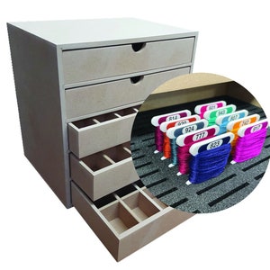 Op de afbeelding: Een lichtgekleurde houten knutselorganizer met vier lades en een bovenste plank. De lades hebben gebogen handgreepuitsparingen. Een cirkelvormige inzet toont kleurrijke borduurgarenspoelen met genummerde labels.
