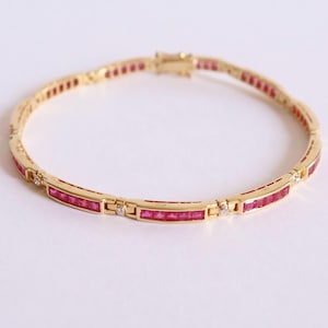 May include: A gold bracelet featuring rectangular red gemstones and small diamonds. The bracelet has a delicate design with a clasp closure. The gemstones are evenly spaced along the bracelet's length. The bracelet is made of gold.